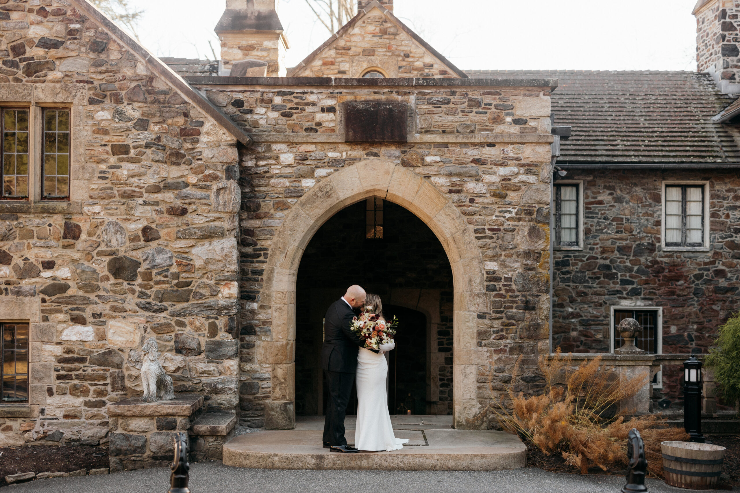 Bride and groom standing in front of a very old rustic building with an arched walkway