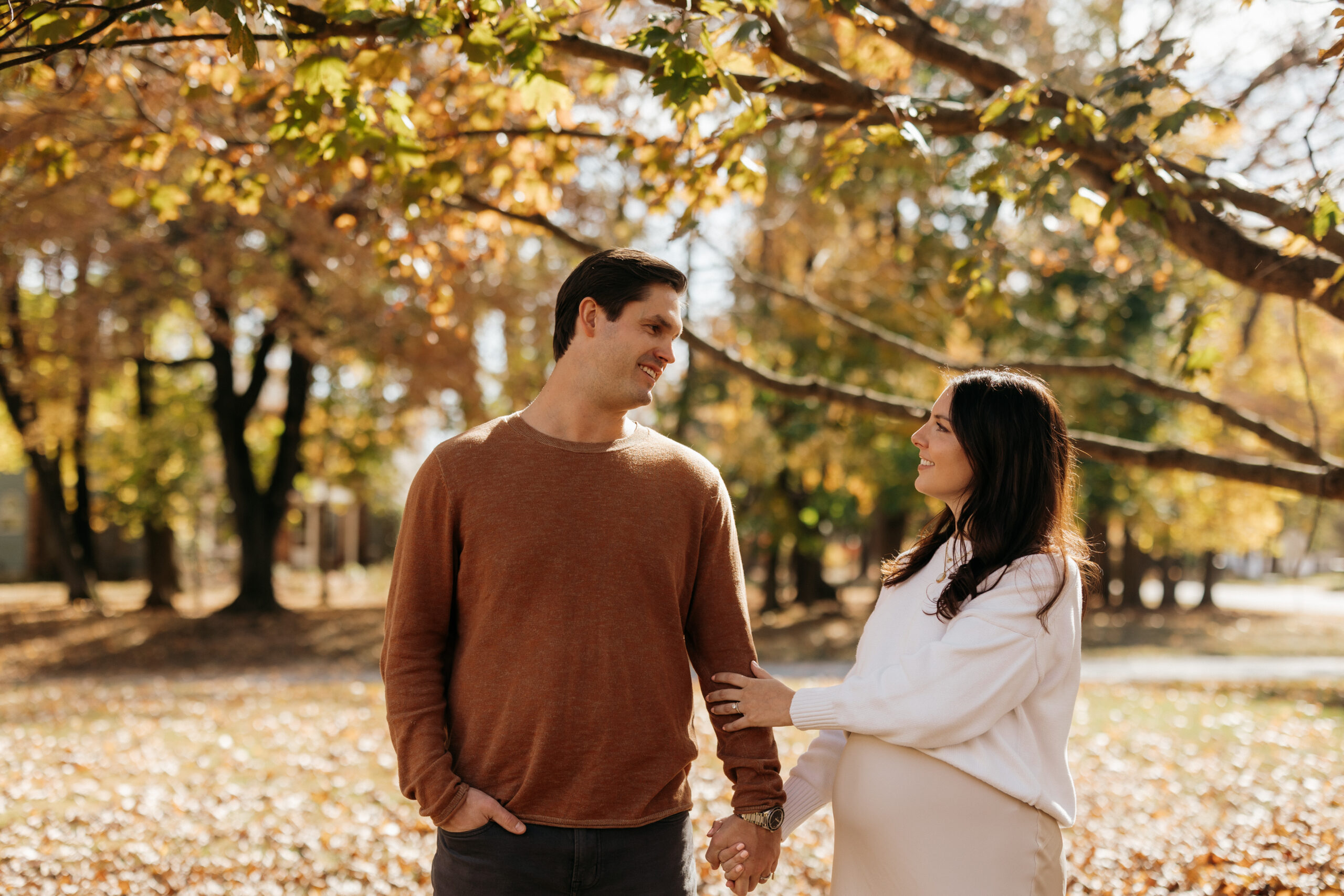 Meredith & Alec are standing in a field of fall leaves looking at one another and holding each others hands.